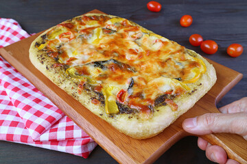 Hand placing delectable fresh baked homemade pesto veggie pizza on the table