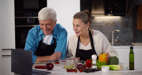 Senior couple using laptop while cooking in kitchen at home