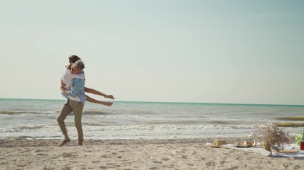 beautiful luaghing joyful man and woman ambracing on beach at seaside and man puts his girlfriend on hands and back like piggyback. lovely couple having fun together at sunny day on sea vacation
