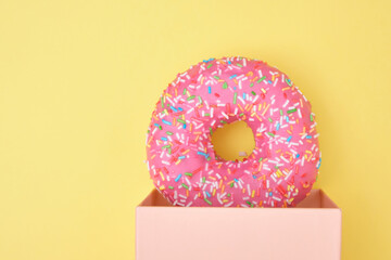 donut with sprinkles and pink icing in a gift box on a yellow background