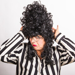 Portrait of mature lady in black high wig and with disgruntled grimace. Carnival lady makeup for party.Facial expressions, characters, role playning.