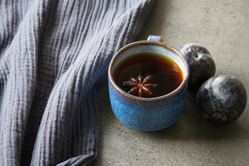 Simple still life in blue colors with ceramic cup and fresh plums. Dark grey background. 
