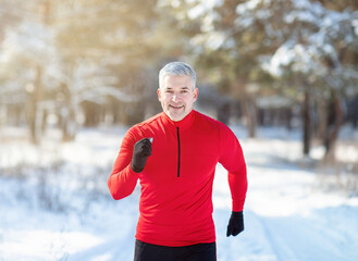 Cross country running in winter. Happy fit senior man jogging in snowy forest on sunny morning