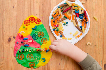 Easter concept. the child places colored noodles on an egg-shaped plasticine. children DIY toys for home ideas, child employment, fine motor skills, ergotherapy, sensory therapy