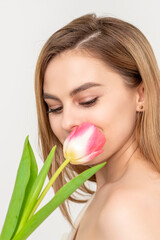 Beautiful caucasian young woman with one tulip looking on a flower against a white background