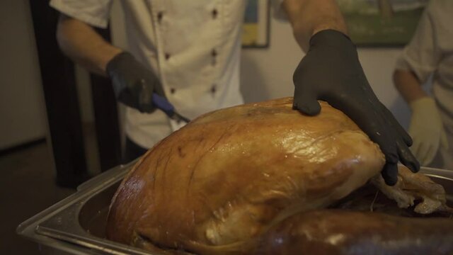Chef with his hands cuts carcass of raw chicken broiler into pieces with kitchen knife. And cut part of chicken breast. Close-up.