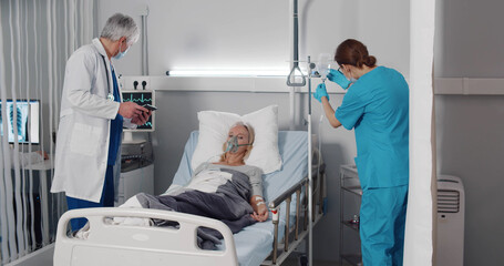 Nurse and doctor standing at hospital bed and checking patient conditions