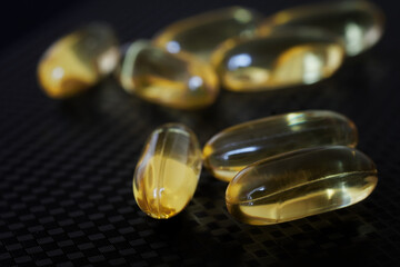 Transparent capsules with fish oil lie on a black textured surface. Medicines and prevention of viral diseases. Selective focus. Macro
