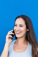 Portrait of a beautiful young woman laughing and talking on the phone with blue wall