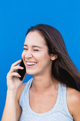 Portrait of a beautiful young woman laughing and talking on the phone with blue wall