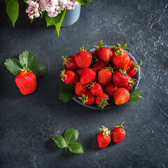 top view macro of strawberries in a gray bowl on a dark textured background with lilac flowers