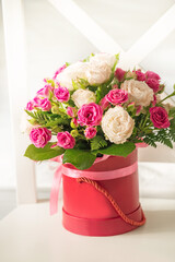 Cute bouquet of pink and beige roses in a red box on a light background.
