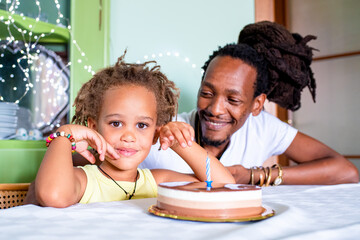 portrait of happy mixed race son and african father, celebration with chocolate cake at home, birthday party of afro descendant kid and rastafarian dad