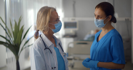 Portrait of doctor and nurse in protective mask and gloves discussing treatment in ward at hospital