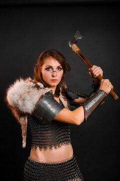 Woman warrior in chain mail armor with lamellar bracers and plate shoulder pad with the fur of a polar fox on her shoulders, stands in a fighting stance with an ax in her hands against dark background