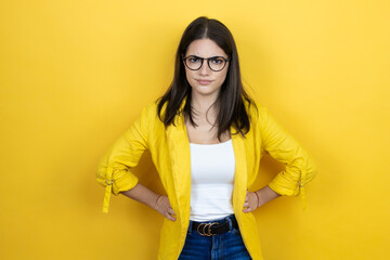 Young brunette businesswoman wearing yellow blazer over yellow background skeptic and nervous,...
