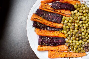 spicy peas and carrots baked in the oven. a delicious vegan meal on black background and blurry view.