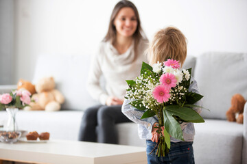 Beautiful blond boy, giving mother flowers and box with little gift for mothers day