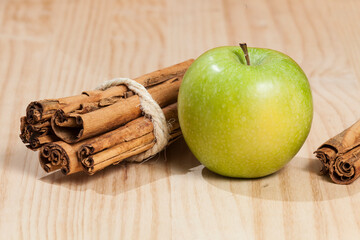 Green apple with a cinnamon stick; photo on wooden background.