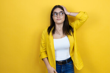 Young brunette businesswoman wearing yellow blazer over yellow background putting one hand on her...