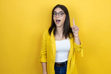 Young brunette businesswoman wearing yellow blazer over yellow background surprised and thinking with her finger on her head that she has an idea.