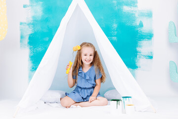 Portrait of a beautiful smiling girl with a paint roller. Little girl playing in a white wigwam on a background of colorful walls. Cheerful cute baby having fun in the nursery. baby's day. © Andriy Medvediuk