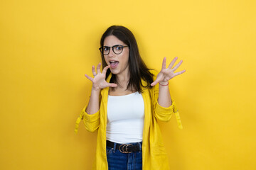 Young brunette businesswoman wearing yellow blazer over yellow background smiling funny doing claw...