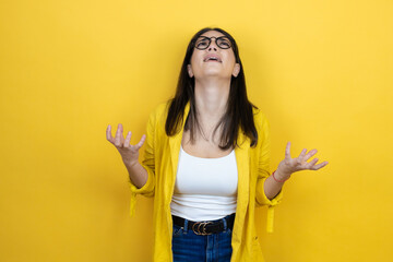 Young brunette businesswoman wearing yellow blazer over yellow background crazy and mad shouting and yelling with aggressive expression and arms raised. Frustration concept.