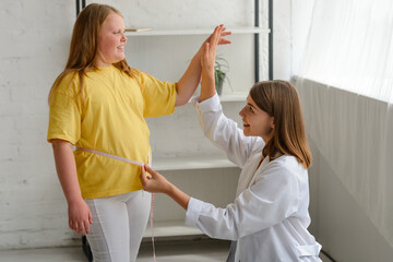 Happy girl losing excess weight. Nutritionist measuring her waistline