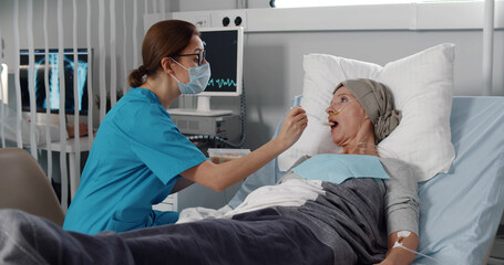 Nurse feeding mature woman having cancer with porridge