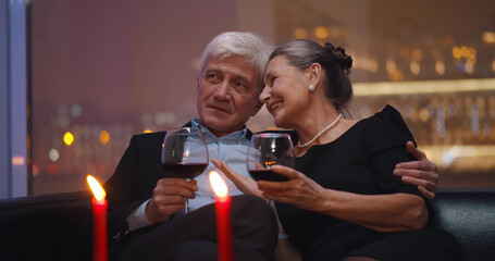 Senior husband and wife drinking red wine relaxing on couch in restaurant