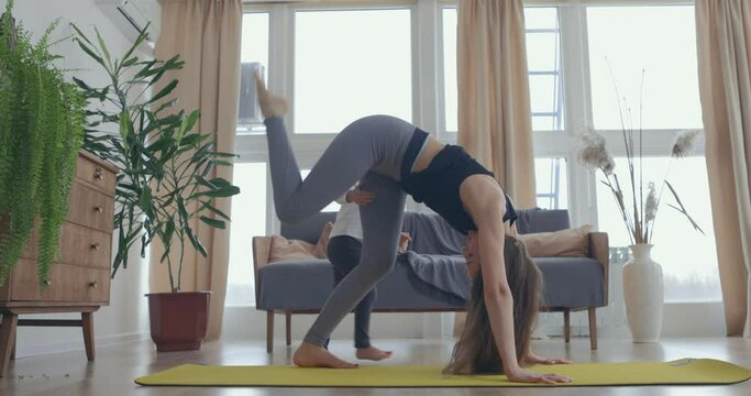 Young beautiful woman and her little baby girl training stretching at home. Mom play fitness with daughter. Slow motion
