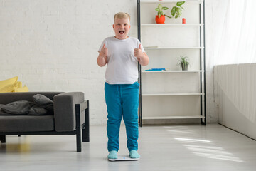 Happy overweight boy after weighing. Cheerful kid showing thumbs up