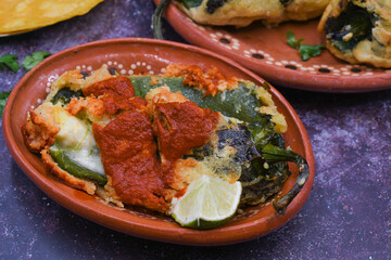 Mexican chiles rellenos stuffed with potato and cheese, vegan batter, served in traditional clay...
