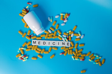 The word of MEDICINE with Pills from a bottle on the blue Background. Selective focus.