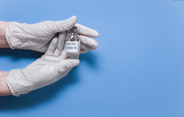 Vaccination concept. Vaccine vial glass bottle for vaccination against COVID-19 SARS-CoV-2 coronavirus pandemic in hands with medical gloves. Top view, flat lay, copy space.