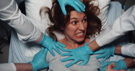 Top view of doctors in latex gloves holding mad screaming woman trying to escape