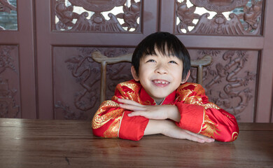 An Asian happy kid with the lovely smiling expression.A Chinese boy in the tradition clothes during Lunar New year festival. A child is sitting on the wooden chair and looking up.