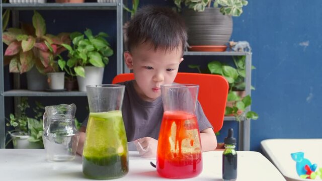 Happy little Asian school kid making DIY Lava Lamp Science Experiment with oil, water and food coloring, Kid-friendly fun and easy science experiments at home concept - slow motion