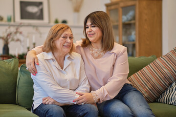 Obraz premium middle aged female visiting her mother, sitting together on comfortable couch, having good conversation. Woman in her forties talking to daughter at home