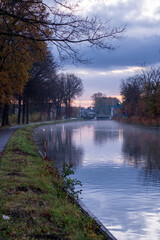 River stream canal bending with grass banks and wild flowers and trees in a scenic landscape on a misty autumns morning sunrise day. High quality photo