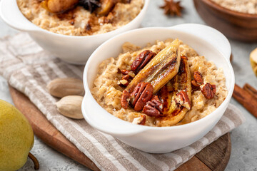 Oatmeal with fried banana, cinnamon, and honey in a white bowl on a gray concrete background close-up. Sweet tasty breakfast.
