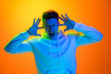 Angry screaming. Caucasian man's portrait isolated on yellow studio background in mixed neon light. Handsome male model. Concept of human emotions, facial expression, sales, ad, fashion. Copyspace.