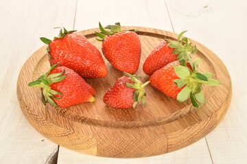 Plenty of juicy strawberries on a round bamboo tray, on a painted wooden table.