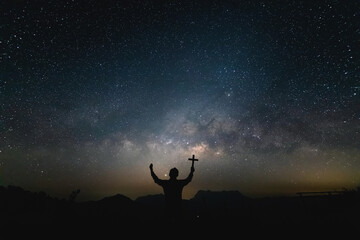 Silhouette Human praying and holding christian cross for worshipping God at Night landscape with colorful Milky Way.