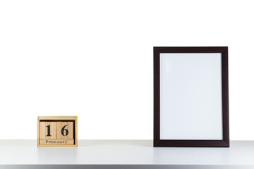 Wooden calendar 16 february with frame for photo on white table and background