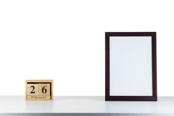 Wooden calendar 26 february with frame for photo on white table and background