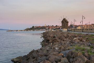 Fototapeta na wymiar Old windmill and ancient town of Nessebar at sunset. View of the windmill, located on a narrow man-made isthmus at the entrance of the UNESCO - protected town of Nessebar, major seaside resort.