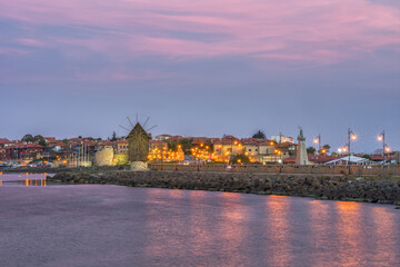 Fototapeta premium Old windmill and citylights at colorful sunset. Amazing view of the windmill, located on a narrow man-made isthmus at the entrance of the UNESCO - protected ancient town of Nessebar, seaside resort.
