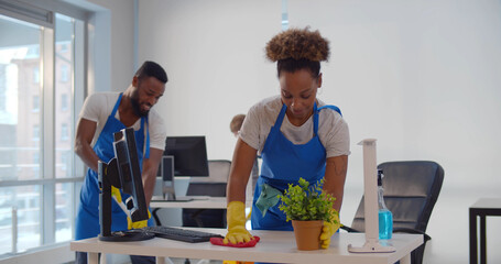 Young diverse male and female cleaners wiping floor and washing furniture in modern office